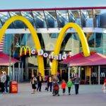 Extérieur du restaurant McDonald's moderne situé près de Disneyland Paris, avec de grandes arches dorées, une façade en verre et des gens se promenant, capturés à la lumière du jour.