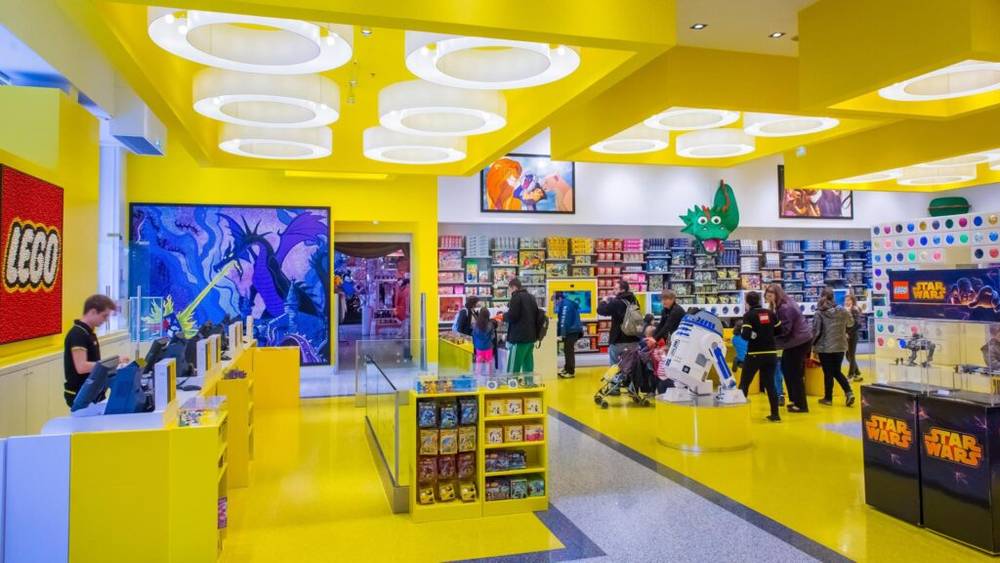 Un Lego Store à Disney Village avec des murs jaunes et des gens qui se promènent.