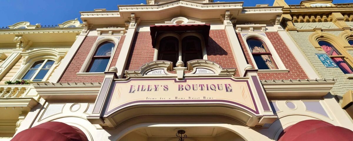 Une image de la façade de la boutique Lilly, présentant une élégante architecture victorienne avec une palette de couleurs pastel. Le panneau et les détails ornés sont mis en valeur sous un ciel bleu clair.
