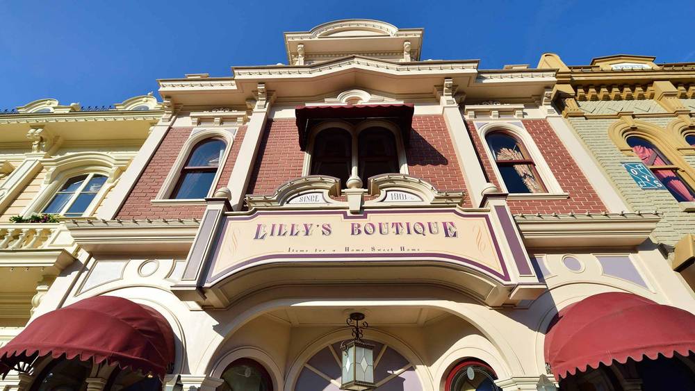 Une image de la façade de la boutique Lilly, présentant une élégante architecture victorienne avec une palette de couleurs pastel. Le panneau et les détails ornés sont mis en valeur sous un ciel bleu clair.