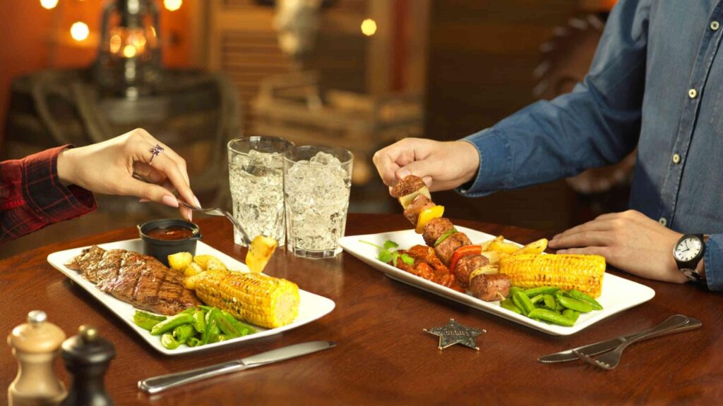 Deux personnes assises à une table dégustant des assiettes de nourriture au Silver Spur Steakhouse à Disneyland Paris.