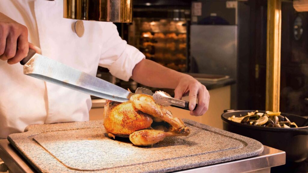 Au restaurant Plaza Gardens de Disneyland Paris, un chef talentueux tranche habilement un poulet frais sur une planche à découper.