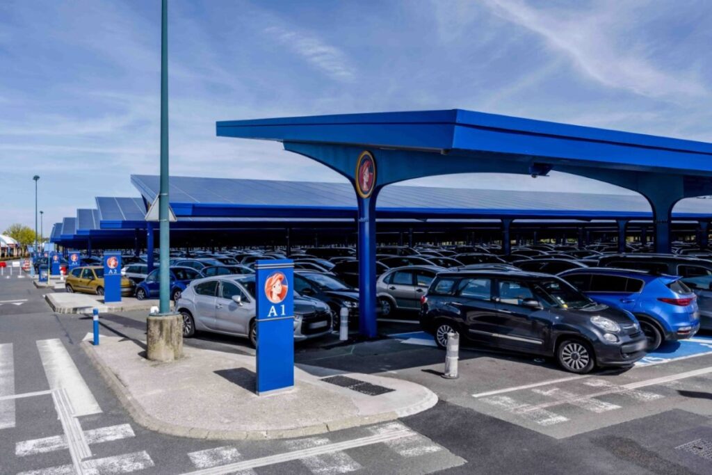 Un parking avec de nombreuses voitures garées sous un auvent bleu, disponible pour stationner à Disneyland Paris à des horaires précis.