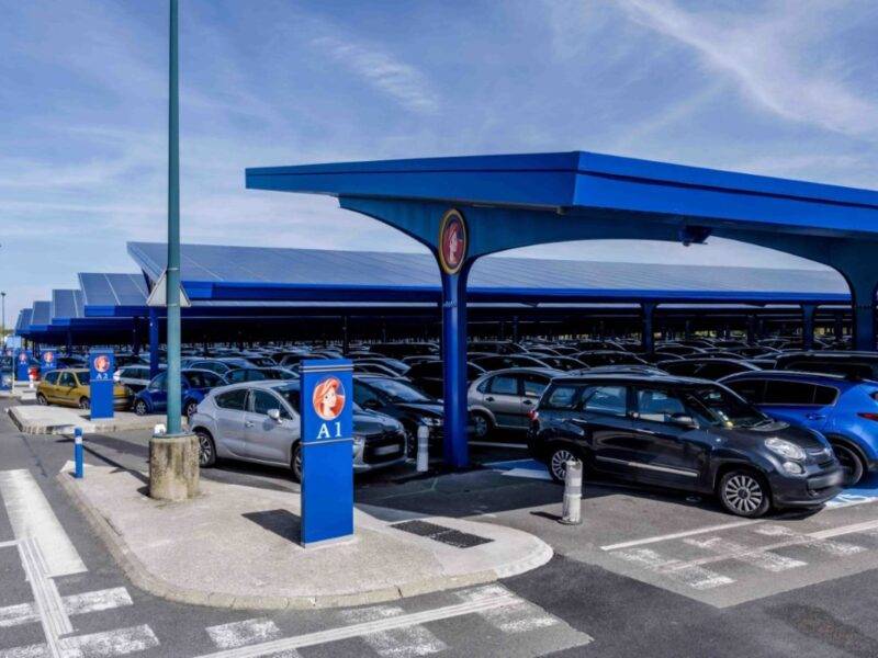 Un parking avec de nombreuses voitures garées sous un auvent bleu, disponible pour stationner à Disneyland Paris à des horaires précis.
