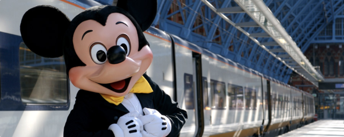 Une mascotte de Disneyland Paris debout à côté d'un train.