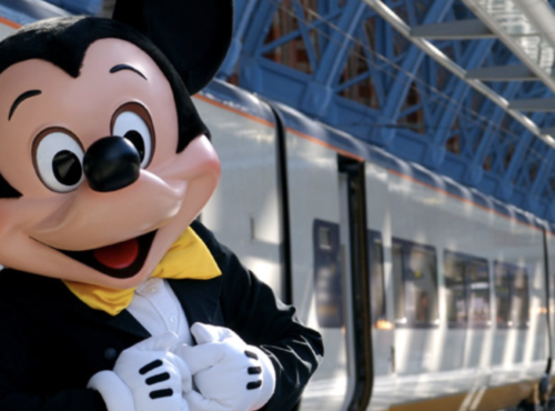 Une mascotte de Disneyland Paris debout à côté d'un train.