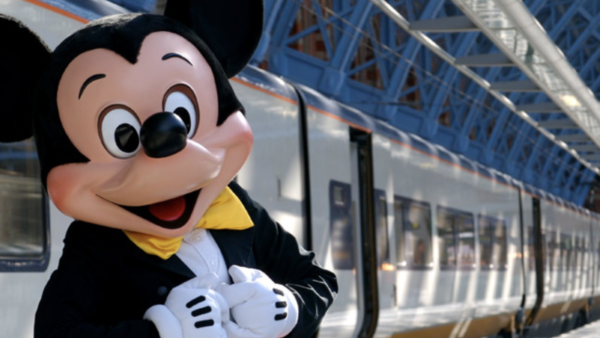 Une mascotte de Disneyland Paris debout à côté d'un train.