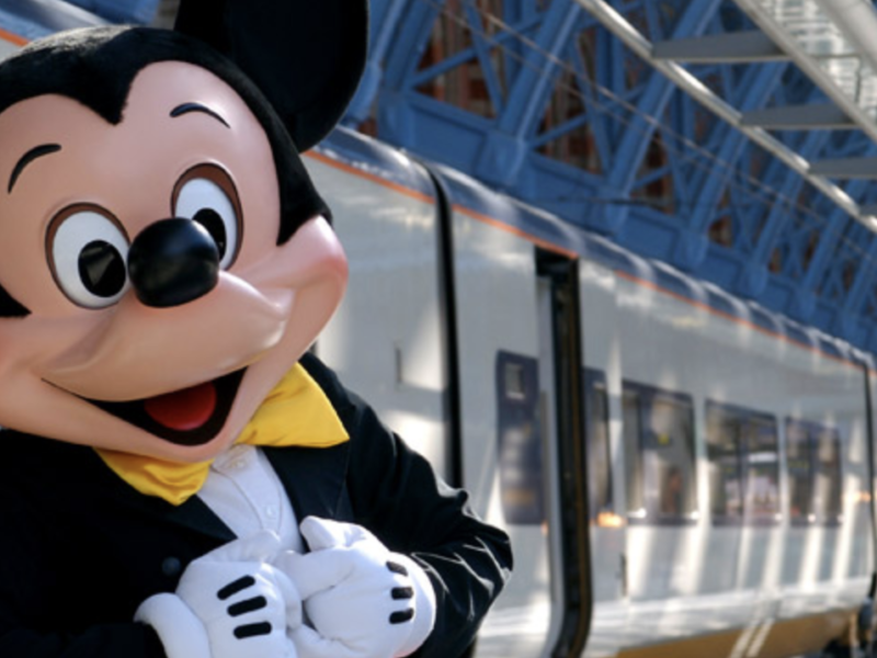 Une mascotte de Disneyland Paris debout à côté d'un train.