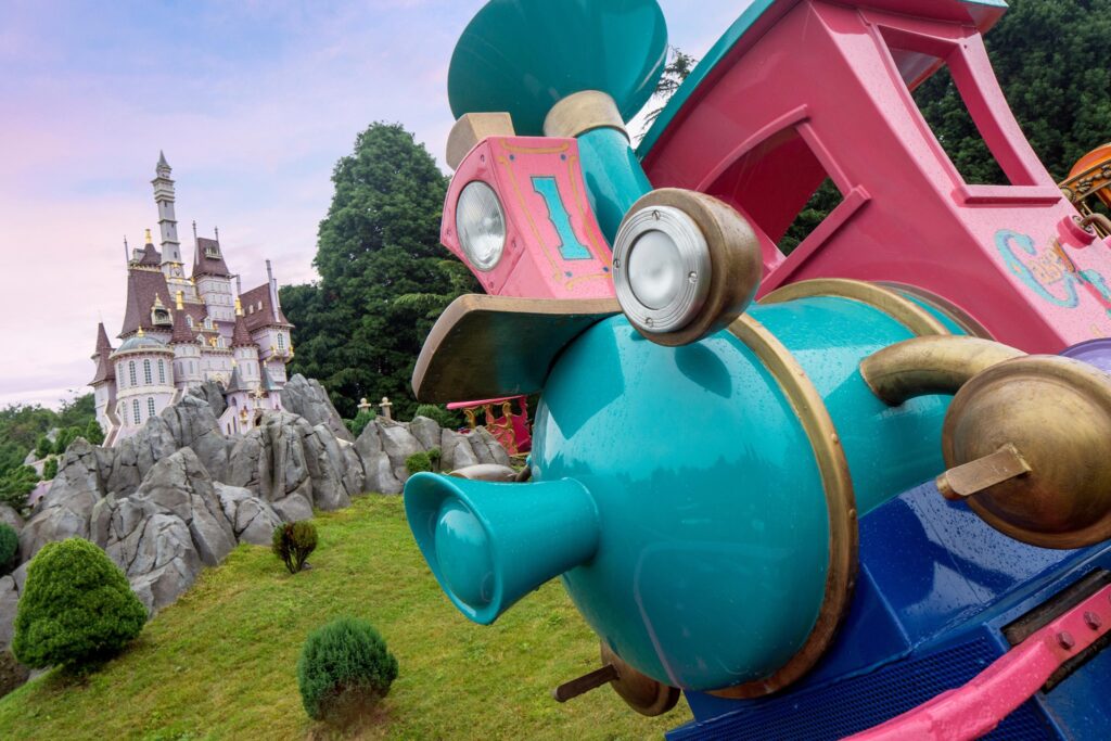 Un train bleu et rose posé devant un château à Disneyland Paris.