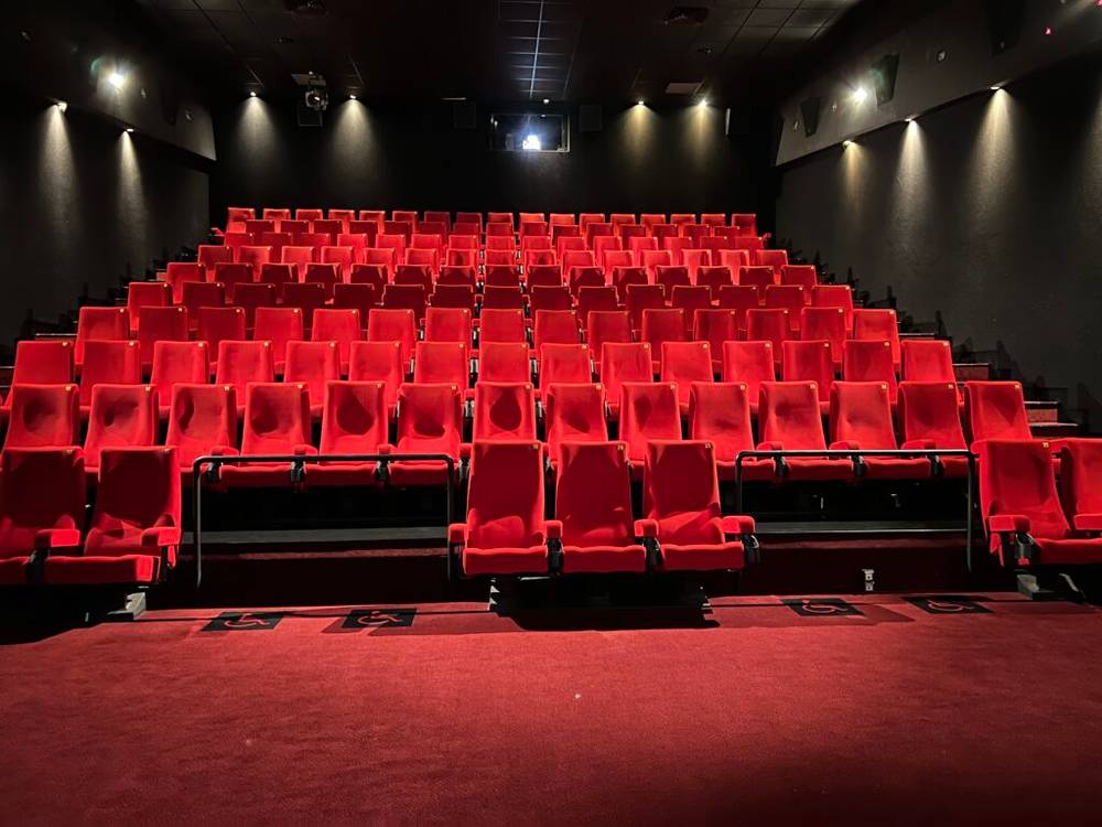 Un cinéma vide avec des sièges rouges et un écran noir attend les cinéphiles.