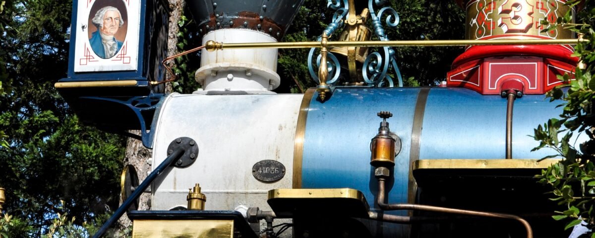 Une locomotive à vapeur colorée vintage du Disneyland Railroad avec des garnitures dorées complexes émet de la vapeur, avec des roues rouges, un corps de moteur bleu et des décorations élaborées sous la lumière du soleil.