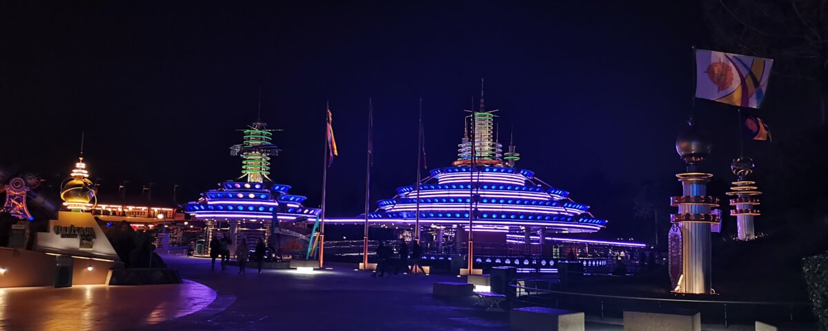Vue nocturne d'une autopie futuriste avec des bâtiments de style pagode éclairés au néon et des drapeaux décoratifs, créant une ambiance vibrante et colorée.