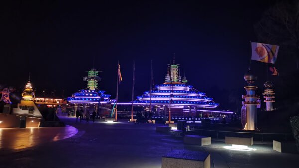 Vue nocturne d'une autopie futuriste avec des bâtiments de style pagode éclairés au néon et des drapeaux décoratifs, créant une ambiance vibrante et colorée.