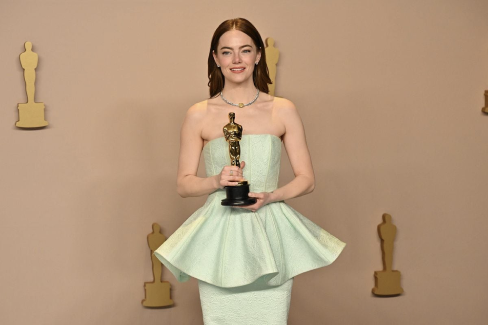 Une femme vêtue d’une robe vert clair tenant une statuette des Oscars.