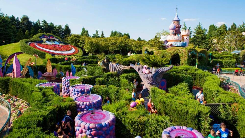 Section de parc d'attractions sur le thème fantastique inspirée du curieux Labyrinthe d'Alice à Disneyland Paris, avec des décorations topiaires et colorées.