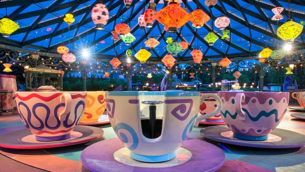 Promenade en tasse de thé colorée à Disneyland Paris au crépuscule avec des lanternes décoratives au-dessus.