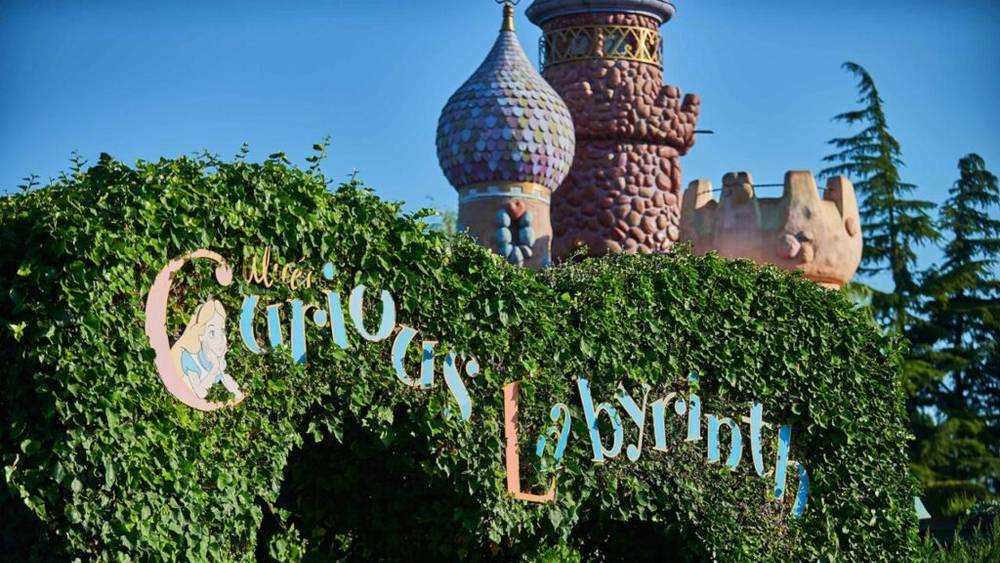 Panneau indiquant l'attraction « L'étrange labyrinthe d'Alice » à Disneyland Paris avec haie et tourelle du château en arrière-plan.