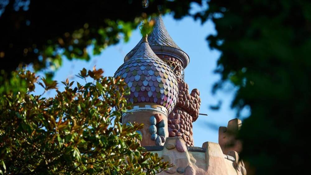 La tourelle du château de conte de fées Alice's Curious Labyrinth jette un coup d'œil à travers un feuillage vert luxuriant sur un ciel bleu clair à Disneyland Paris.