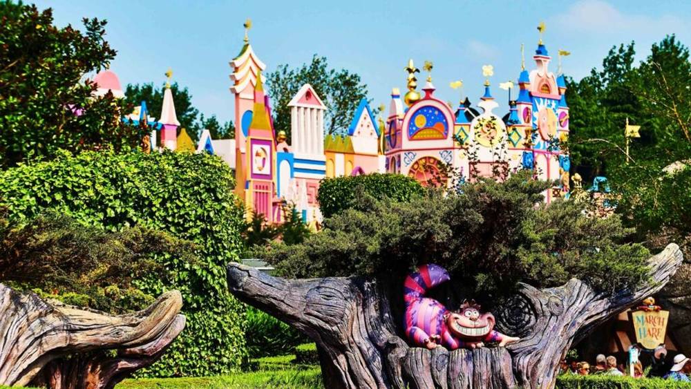 Château de conte de fées coloré à l'architecture fantaisiste derrière une figure de chat du Cheshire dans l'étrange labyrinthe d'Alice à Disneyland Paris.