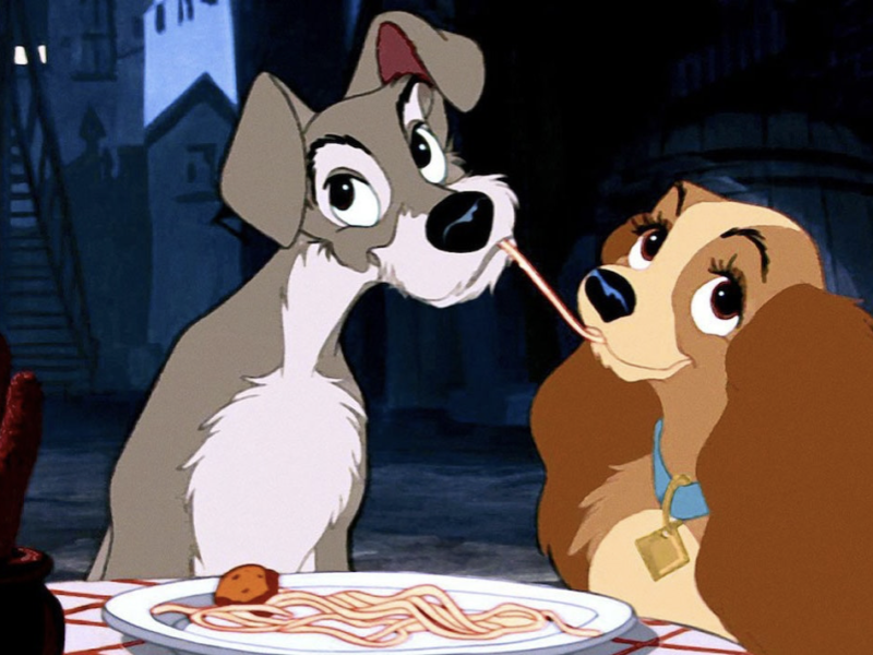 Image animée de La Belle et le Clochard partageant des spaghettis lors d'un dîner aux chandelles, leurs nez se rencontrant au milieu alors qu'ils mangent le même brin de pâtes.