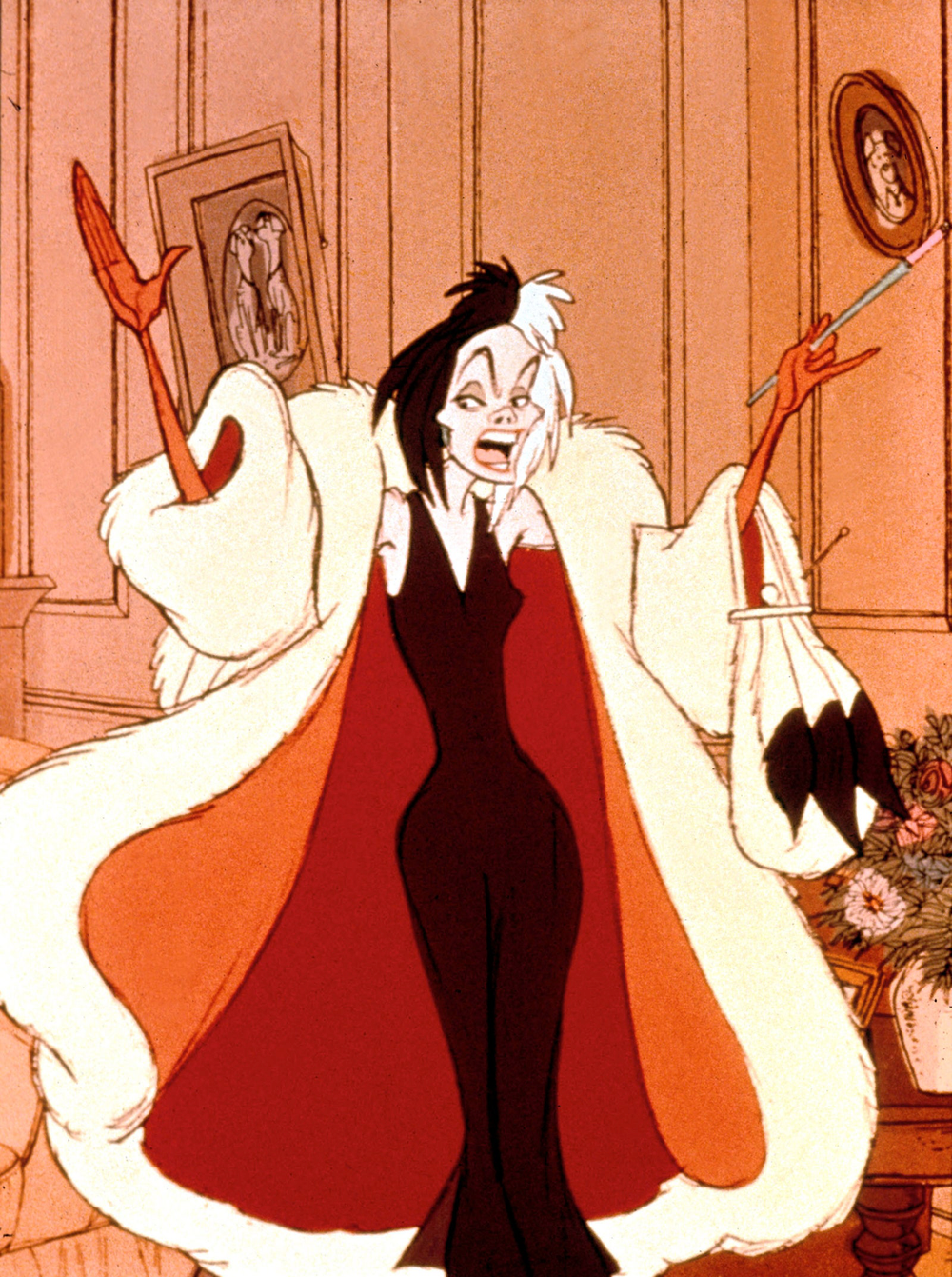 Le personnage animé Cruella de Vil se tient dans une pièce, souriant méchamment, avec ses cheveux noirs et blancs ébouriffés. Elle porte un somptueux manteau de fourrure et une robe rouge, tenant un sac à main et un
