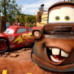 Des modèles grandeur nature de Lightning McQueen et Mater du film Disney's Cars exposés dans un parc à thème à Disneyland Paris, avec des détails vibrants et des arrière-plans colorés.