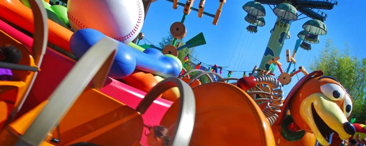 Manège coloré à Disneyland Paris inspiré par l'esthétique du jouet, avec des finitions en plastique brillant et des designs fantaisistes avec un motif de balle de baseball et de batte. Des montagnes russes et des toboggans sont visibles en arrière-plan.