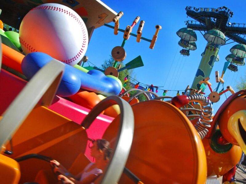 Manège coloré à Disneyland Paris inspiré par l'esthétique du jouet, avec des finitions en plastique brillant et des designs fantaisistes avec un motif de balle de baseball et de batte. Des montagnes russes et des toboggans sont visibles en arrière-plan.