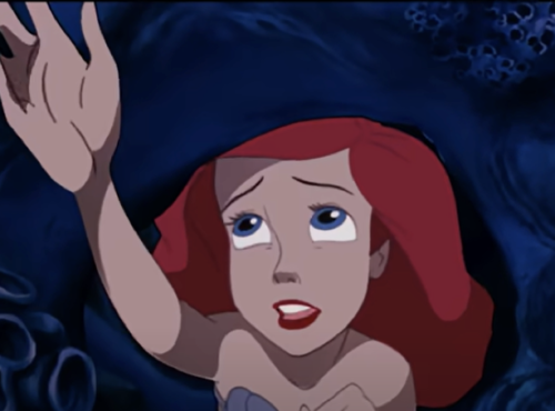 Image animée d'Ariel de "La Petite Sirène", regardant vers le haut avec une expression inquiète, la main tendue, sur un fond sous-marin sombre.