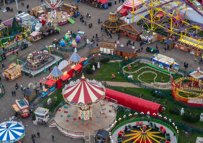 Vue aérienne d'un parc d'attractions coloré avec divers manèges, jeux de carnaval et de nombreuses personnes se promenant, rappelant les meilleurs parcs d'attractions de France.