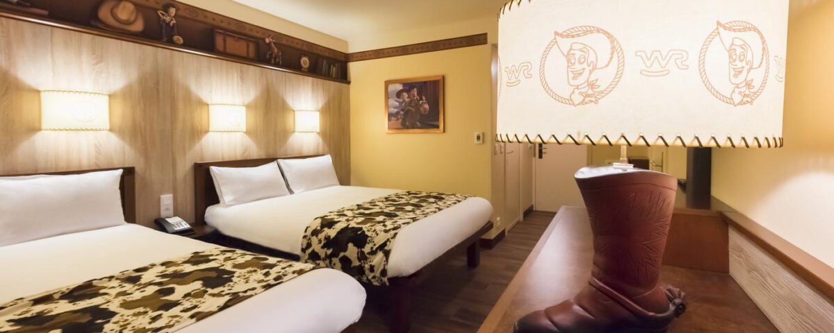 Chambre d'hôtel avec deux lits doubles, plaids à imprimé vache, lampe en forme de botte et abat-jour à thème cow-boy. Des éléments de décoration Disney/Pixar ornent le mur de cet espace charmant inspiré de Cheyenne.