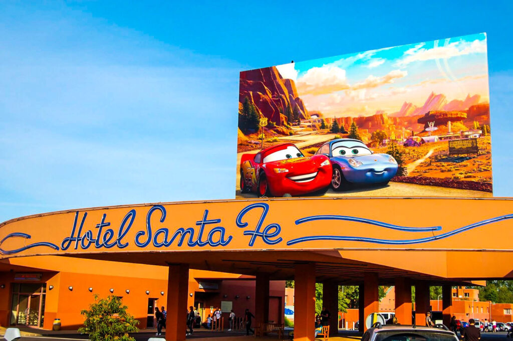 Panneau de l'hôtel Santa Fe avec un grand panneau publicitaire sur le thème du film Cars mettant en vedette les personnages animés Lightning McQueen et Sally Carrera sur le dessus. Le ciel bleu vif en arrière-plan vous invite à démarrer votre moteur et à vous lancer vers l'aventure le long du Rio Grande.