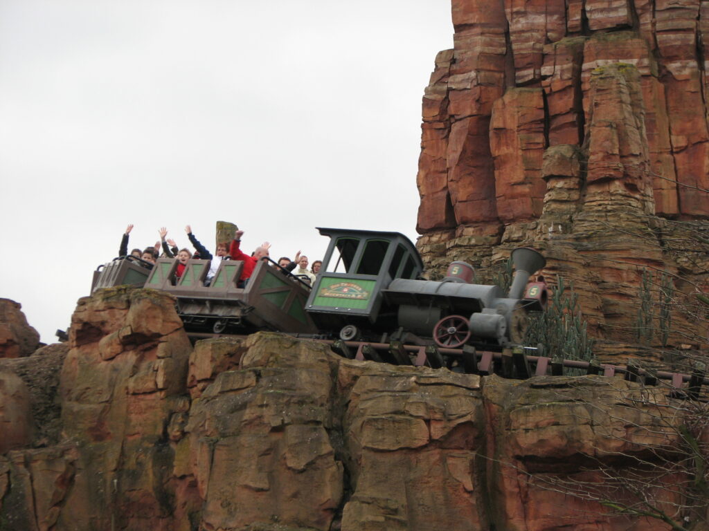 Un groupe de personnes monte sur les montagnes russes du train minier Big Thunder Mountain sur une piste construite dans une falaise rocheuse.