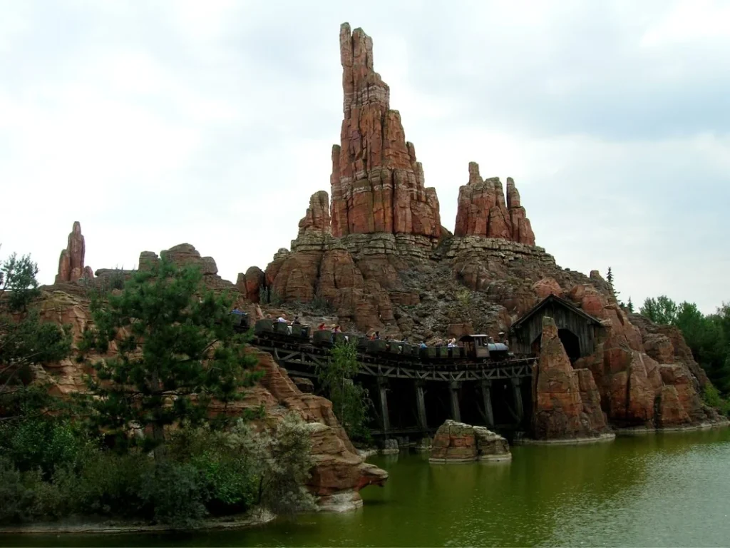 Vivez le frisson de Big Thunder Mountain sur des montagnes russes sur le thème des Rocheuses, avec une voie ferrée serpentant à travers de superbes formations rocheuses rouges, entourées d'une verdure luxuriante et d'eau scintillante.