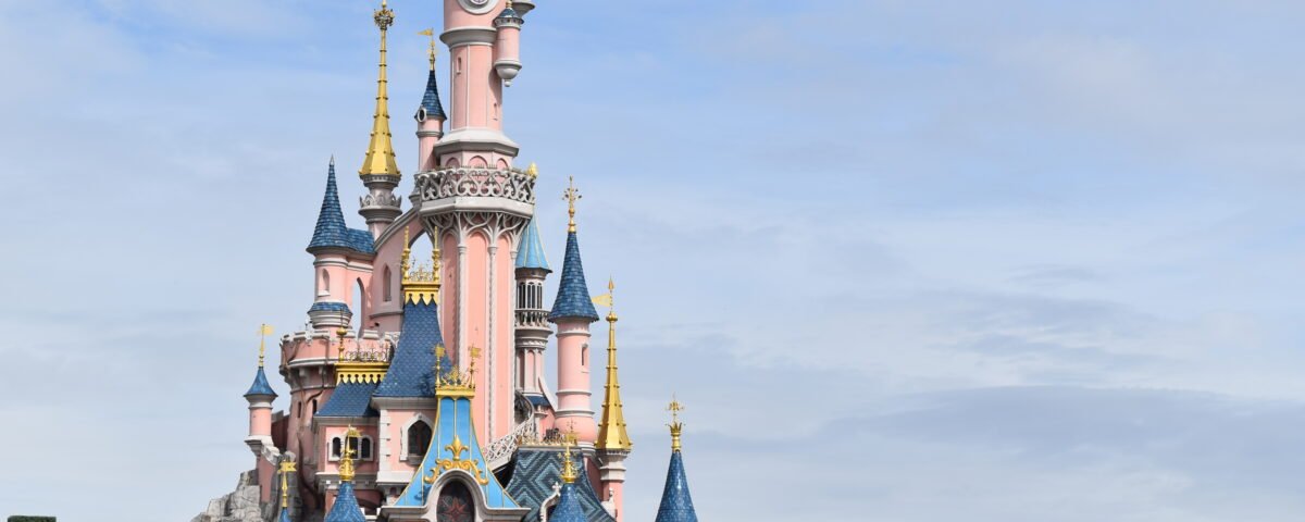 Un château coloré et orné avec plusieurs flèches et des détails complexes, sur fond de ciel partiellement nuageux dans le Parc Disneyland.