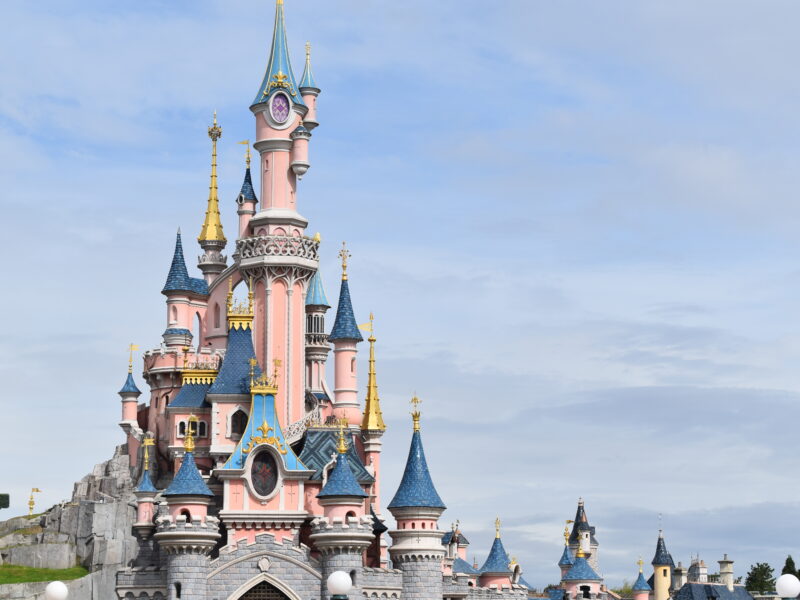 Un château coloré et orné avec plusieurs flèches et des détails complexes, sur fond de ciel partiellement nuageux dans le Parc Disneyland.