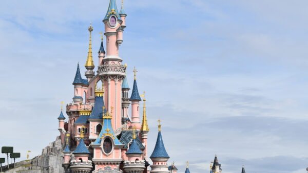 Un château coloré et orné avec plusieurs flèches et des détails complexes, sur fond de ciel partiellement nuageux dans le Parc Disneyland.