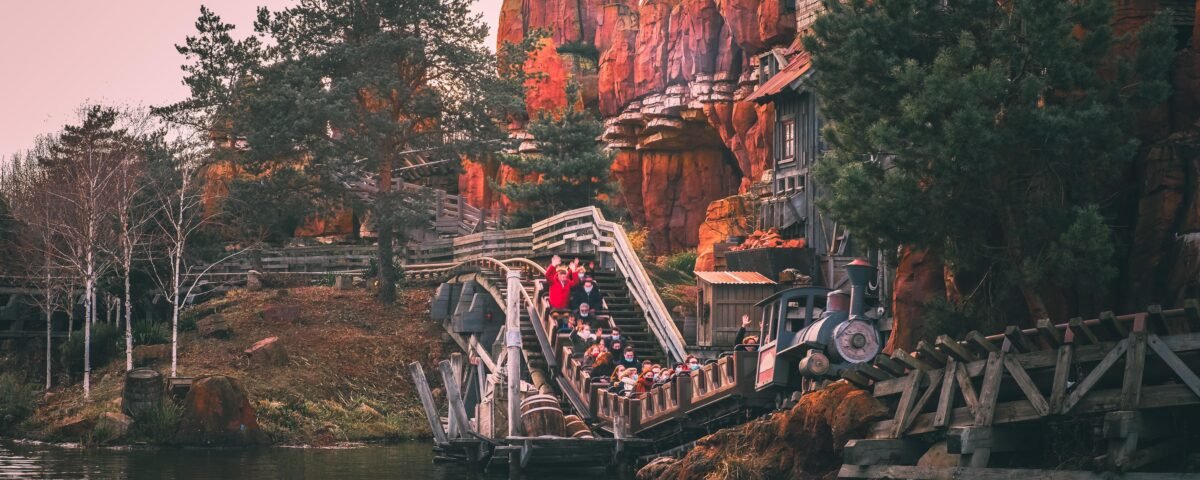 Les gens montent à bord d'un train de montagnes russes Big Thunder Mountain à travers un paysage rocheux et montagneux avec des arbres et de l'eau au premier plan.