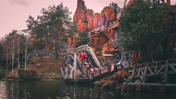 Les gens montent à bord d'un train de montagnes russes Big Thunder Mountain à travers un paysage rocheux et montagneux avec des arbres et de l'eau au premier plan.