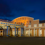 Vue nocturne d'une place de ville à thème western, avec un bâtiment étiqueté « Hôtel Cheyenne Disney » et un « Magasin général », avec des guirlandes lumineuses illuminant la zone, promettant un séjour mémorable.