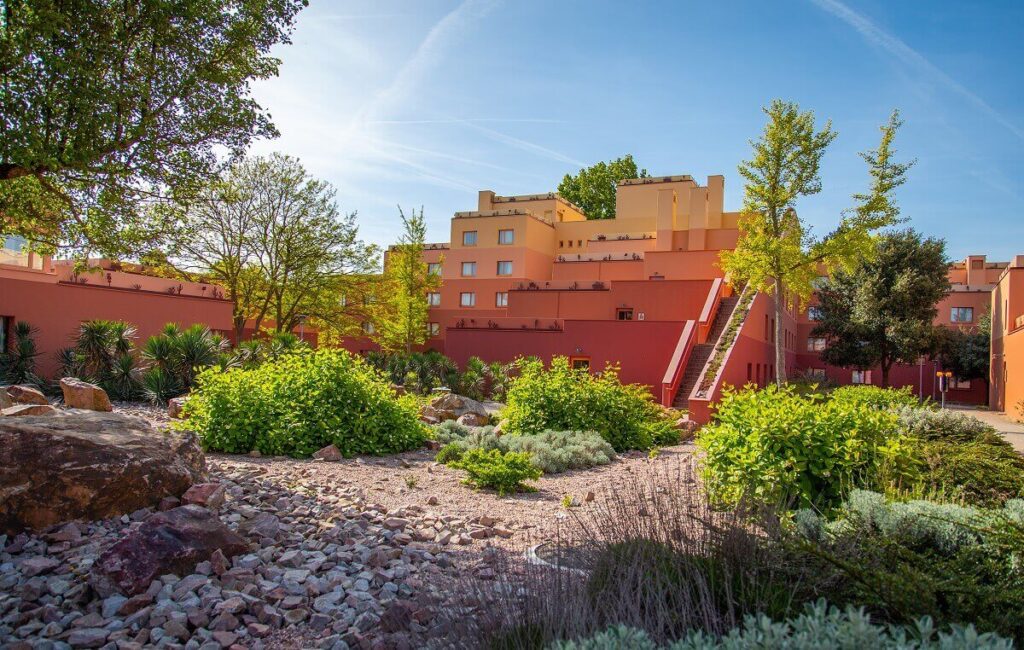 Un complexe d'appartements coloré avec des bâtiments jaunes et rouges est entouré d'une verdure luxuriante et d'un paysage rocheux sous un ciel bleu clair, rappelant l'ambiance vibrante que vous trouverez à Rio Grande.