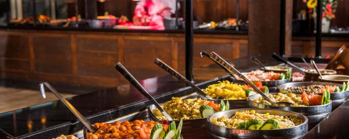 Une table de buffet est dressée avec divers plats, notamment des légumes, des fruits de mer et de la viande. Un chef découpe de la viande en arrière-plan. Découvrez ce festin gastronomique dans le meilleur lieu de restauration de Disney Village en 2024.