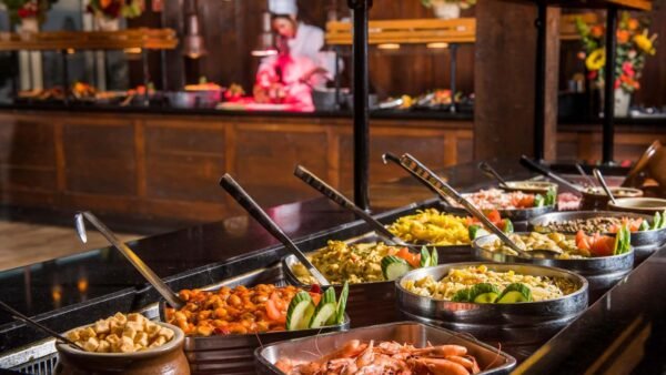 Une table de buffet est dressée avec divers plats, notamment des légumes, des fruits de mer et de la viande. Un chef découpe de la viande en arrière-plan. Découvrez ce festin gastronomique dans le meilleur lieu de restauration de Disney Village en 2024.