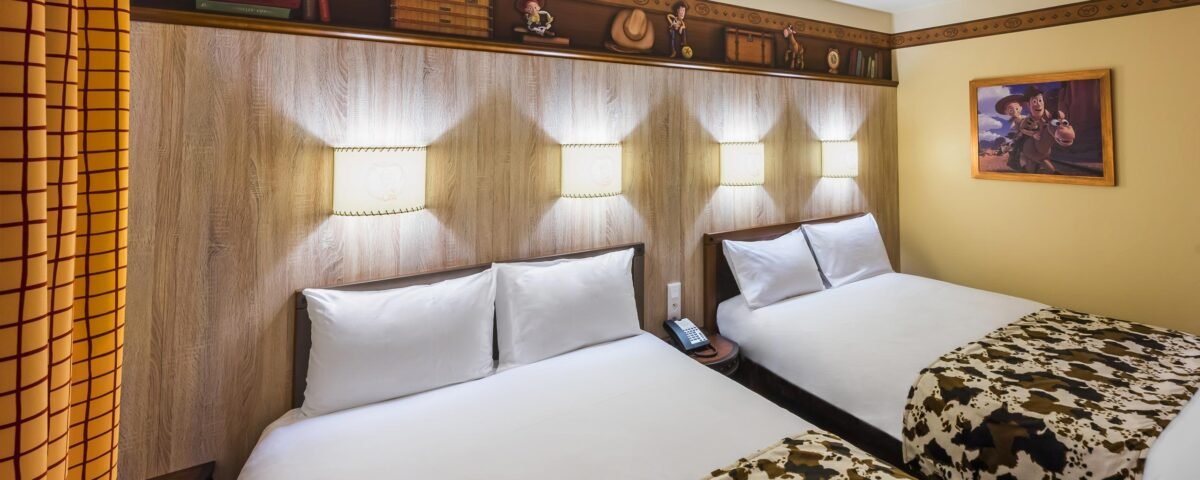 Une chambre d'hôtel sur le thème de Cheyenne avec deux lits doubles soigneusement faits, chacun doté de draps blancs et de couvertures à imprimé vache. Les murs sont ornés d'éléments sur le thème de l'Ouest, notamment des tableaux et des étagères.