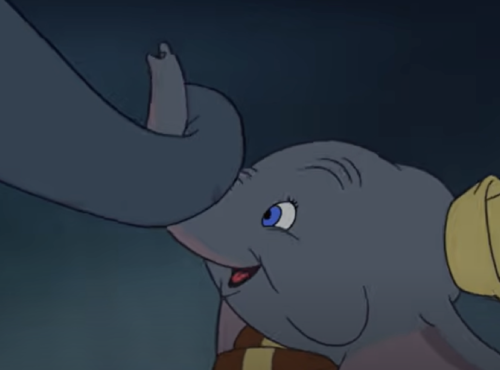 Un jeune éléphant de dessin animé aux grandes oreilles, coiffé d'un chapeau jaune, tient délicatement la trompe d'un autre éléphant avec son propre « mon tout petit », sur fond sombre.