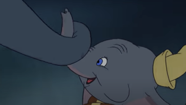 Un jeune éléphant de dessin animé aux grandes oreilles, coiffé d'un chapeau jaune, tient délicatement la trompe d'un autre éléphant avec son propre « mon tout petit », sur fond sombre.