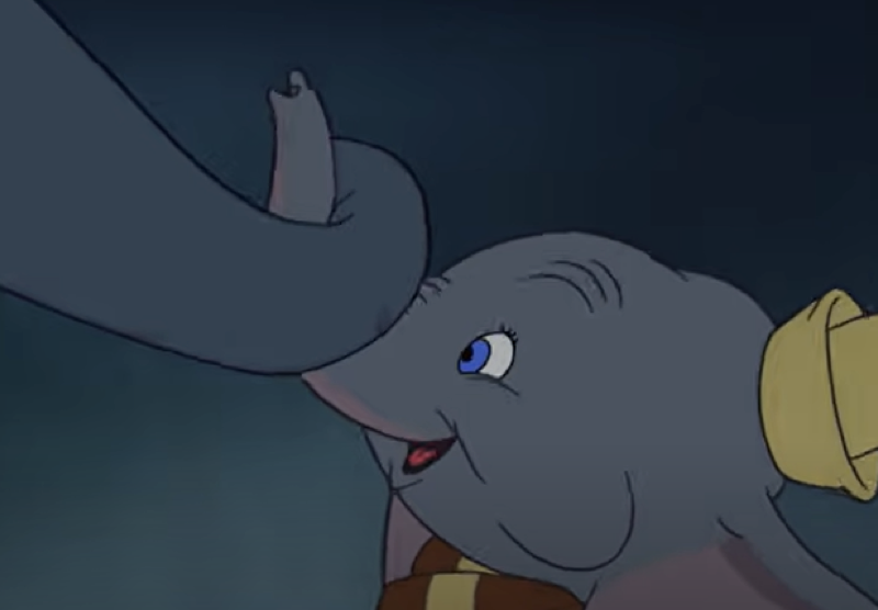 Un jeune éléphant de dessin animé aux grandes oreilles, coiffé d'un chapeau jaune, tient délicatement la trompe d'un autre éléphant avec son propre « mon tout petit », sur fond sombre.