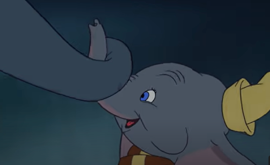 Un jeune éléphant de dessin animé aux grandes oreilles, coiffé d'un chapeau jaune, tient délicatement la trompe d'un autre éléphant avec son propre « mon tout petit », sur fond sombre.