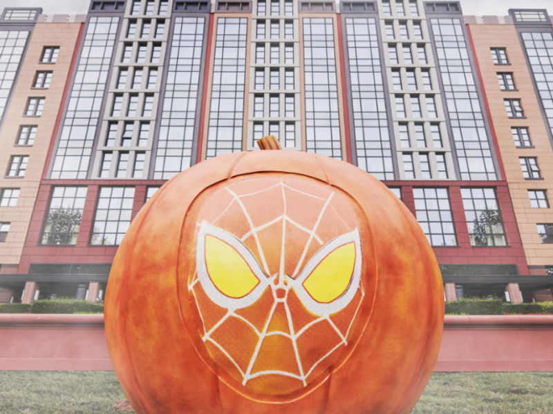 Grande citrouille avec un motif de masque d'araignée stylisé sur le devant, placée devant un bâtiment moderne à plusieurs étages, capturant l'esprit enchanteur du Mode Halloween que vous trouverez à Disneyland.