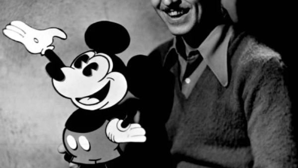 Une personne est assise à côté d'une découpe de Mickey Mouse, souriant à la caméra, célébrant avec joie la naissance du personnage bien-aimé le 18 novembre 1928.